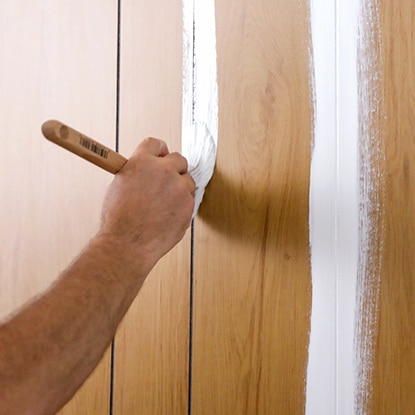 A homeowner brushes primer into the grooves of wood paneling. A homeowner brushes primer into the grooves of wood paneling.