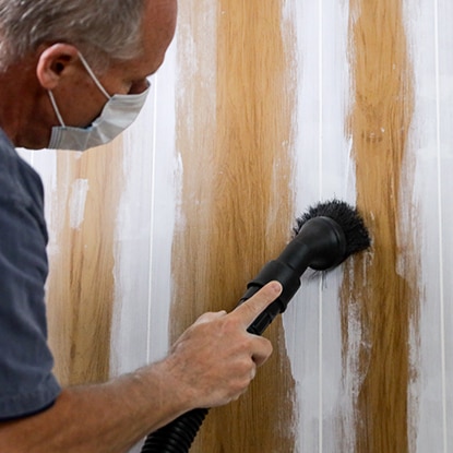 A homeowner wearing a dust mask sands the caulked grooves of wood paneling. A homeowner wearing a dust mask sands the caulked grooves of wood paneling.