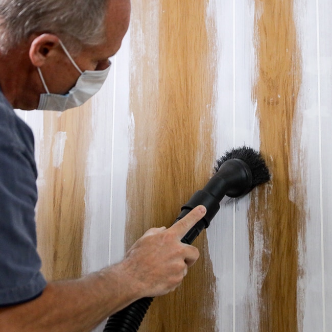 A homeowner wearing a dust mask sands the caulked grooves of wood paneling. A homeowner wearing a dust mask sands the caulked grooves of wood paneling.
