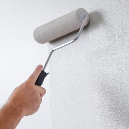 A homeowner finishes rolling white paint onto a wood paneled wall. A homeowner finishes rolling white paint onto a wood paneled wall.