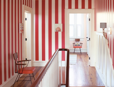 Hallway with red- and white-stripe painted walls, midcentury chair, funky wall art, white trim and wainscoting, and stairs. Hallway with red- and white-stripe painted walls, midcentury chair, funky wall art, white trim and wainscoting, and stairs.