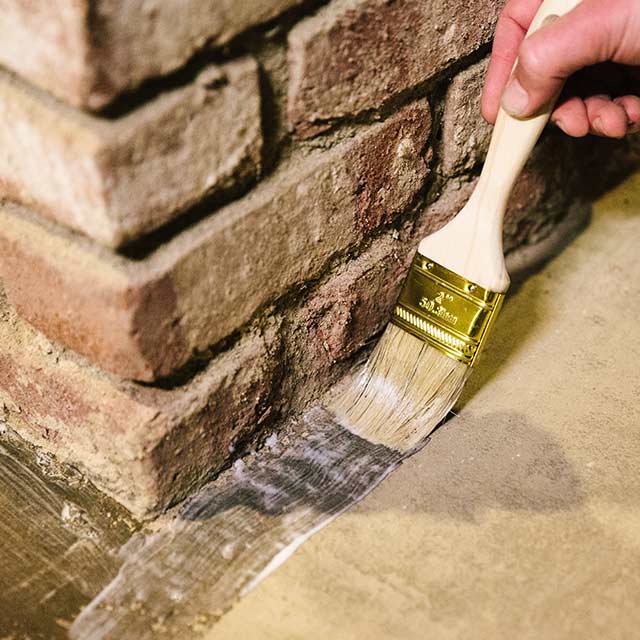 A homeowner applies sealer to a floor using a paintbrush. A homeowner applies sealer to a floor using a paintbrush.