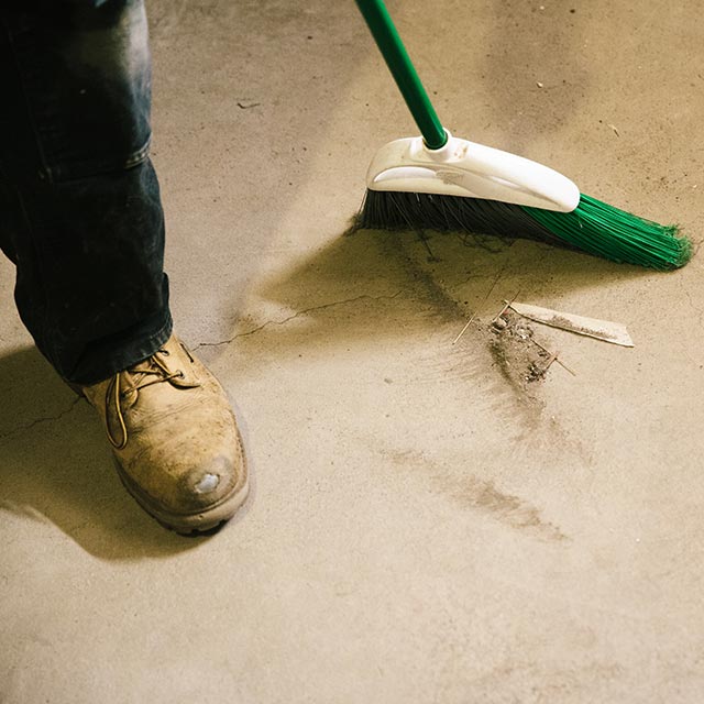 A homeowner sweeps dust and dirt from a concrete floor using a green broom. A homeowner sweeps dust and dirt from a concrete floor using a green broom.
