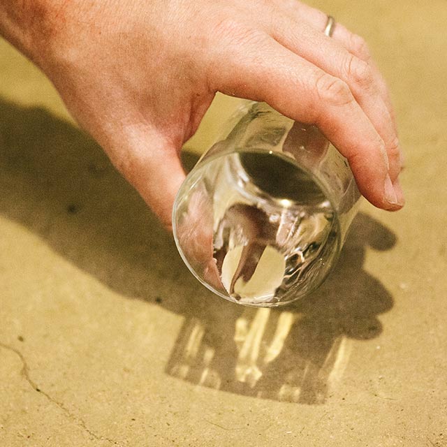 A homeowner tests a concrete floor by pouring a few drops of water from a small glass onto the floor. A homeowner tests a concrete floor by pouring a few drops of water from a small glass onto the floor.
