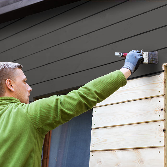 Man painting home exterior a rich black. Man painting home exterior a rich black.