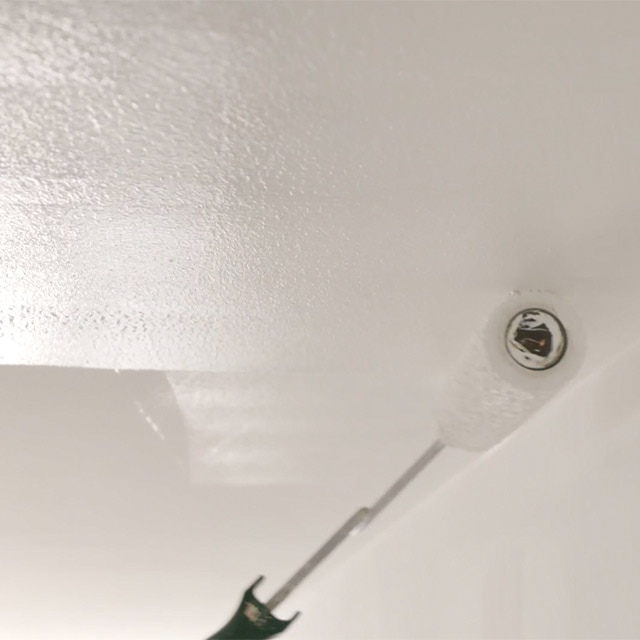 A closeup of white paint being rolled onto a ceiling. A closeup of white paint being rolled onto a ceiling.