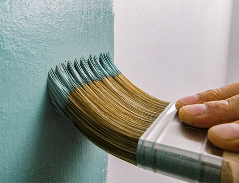 A homeowner using a brush to paint a wall teal.