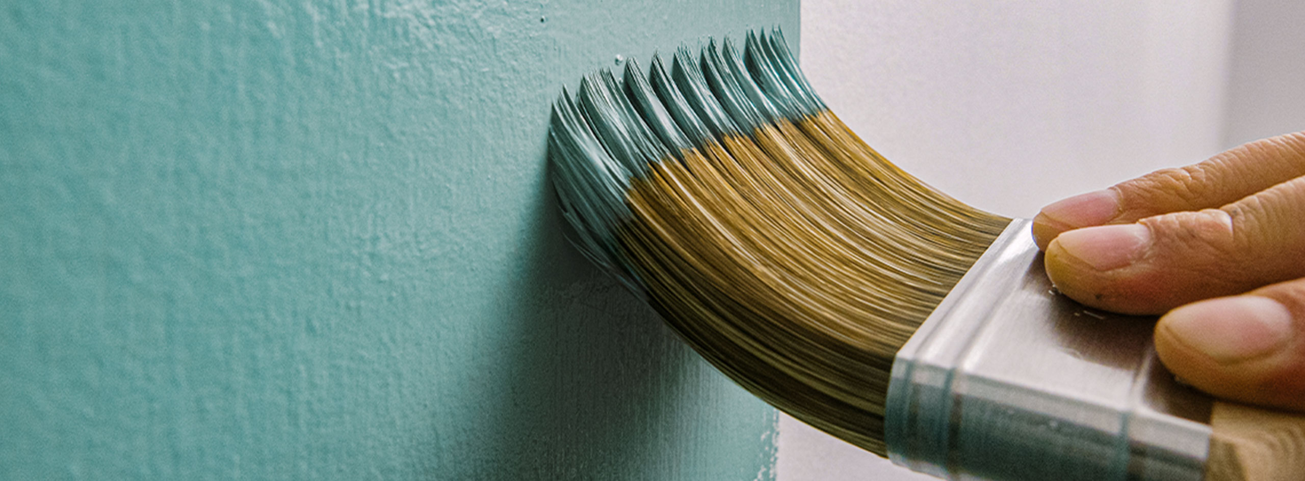 A homeowner using a brush to paint a wall teal. A homeowner using a brush to paint a wall teal.