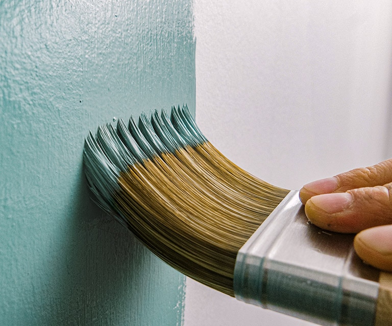 A homeowner using a brush to paint a wall teal. A homeowner using a brush to paint a wall teal.