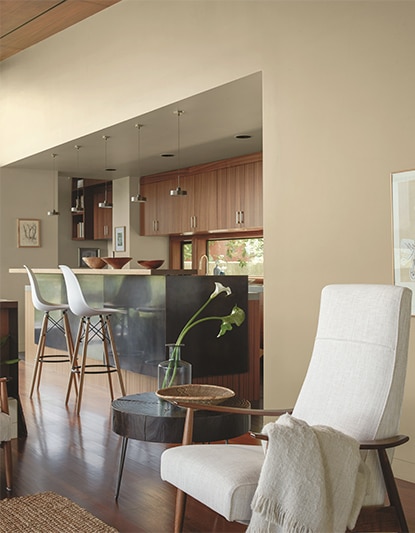 White cushioned chair in lounge area next to kitchen with tan walls and wood cabinets. White cushioned chair in lounge area next to kitchen with tan walls and wood cabinets.
