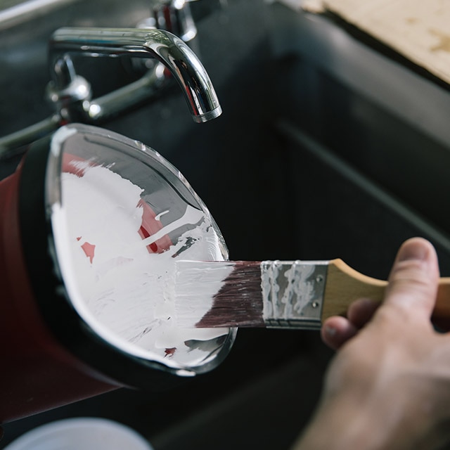 Removing excess paint from the brush by pressing it against the inside lip of the paint can. Removing excess paint from the brush by pressing it against the inside lip of the paint can.