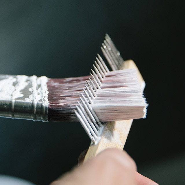 A person removes excess water from a paintbrush by using a brush comb. A person removes excess water from a paintbrush by using a brush comb.