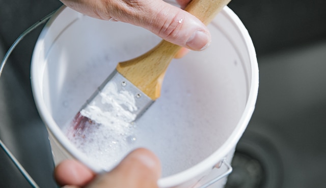 A close up of soaking paintbrush in a bucket of soapy water. A close up of soaking paintbrush in a bucket of soapy water.