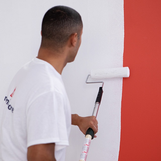 A painting contractor rolls Fresh Start® primer over a red-painted wall. A painting contractor rolls Fresh Start® primer over a red-painted wall.