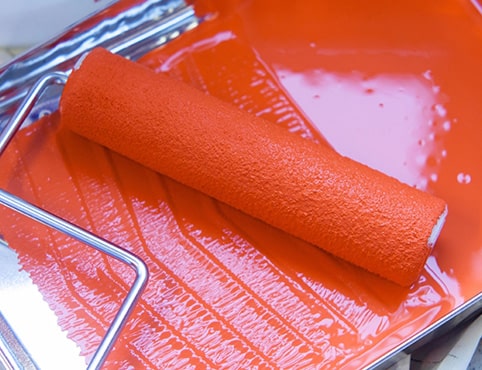 A roller cover resting in a roller tray coated with red paint A roller cover resting in a roller tray coated with red paint