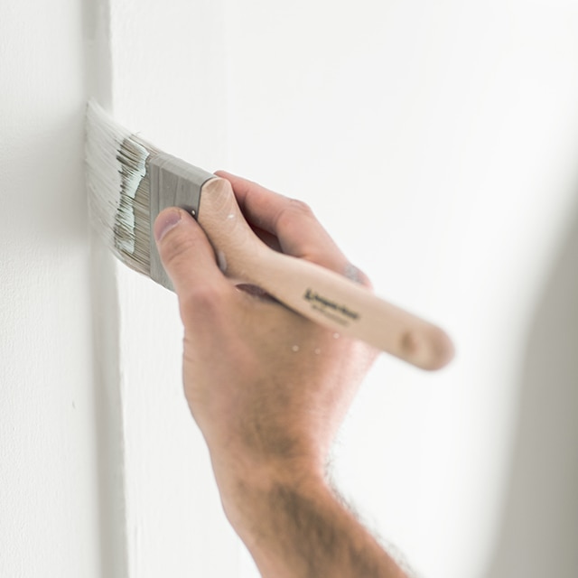 A hand holding a paintbrush paints a wall with white paint. A hand holding a paintbrush paints a wall with white paint.