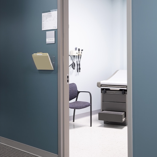 A blue painted-hallway with gray trim in a medical office, looking into a pristine exam room. A blue painted-hallway with gray trim in a medical office, looking into a pristine exam room.