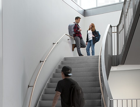 A multi-story staircase with gray-painted walls, large windows, and a man and woman standing on the landing. A multi-story staircase with gray-painted walls, large windows, and a man and woman standing on the landing.